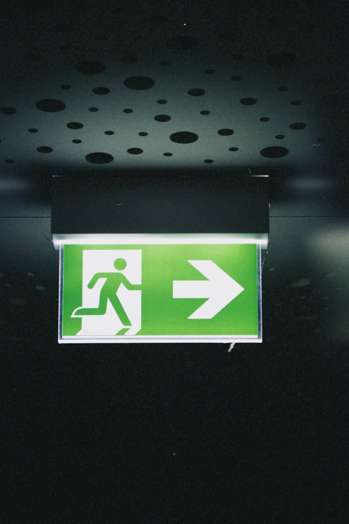 who-we-are Green emergency exit sign with arrow directing to the right, located indoors.