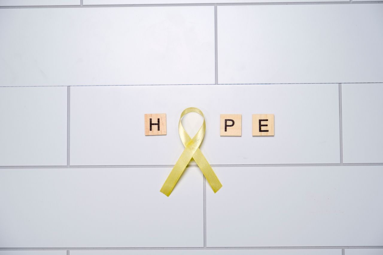 team-03 A yellow ribbon forming the word 'hope' with tiles on a white tiled background, symbolizing awareness and support.