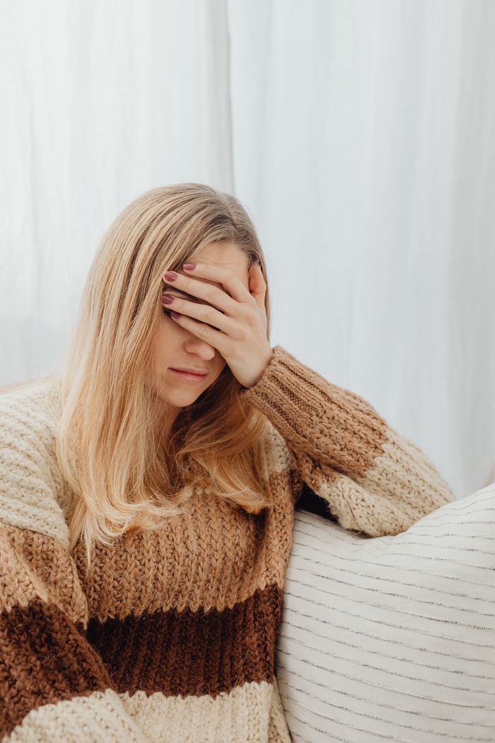 team-04 A woman in a warm sweater covers her face, appearing unwell while sitting indoors.
